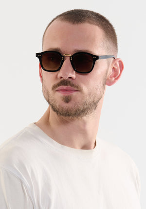CAMPBELL | Black + Black Tea 18K Handcrafted, luxury black acetate medium round KREWE sunglasses with gold stainless steel metal hardware mens model | Model: Connor